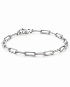 The Aelin Paperclip Bracelet in polished silver tone, low-angle complete oval resting view with the marked clasp toward the upper-left on a plain pearl-white studio surface; reference-based AI visualization