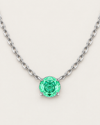 Round green faceted pendant in a silver-colored four-prong setting suspended from a wide linked-chain arc on pale greige — reference-based AI visualization