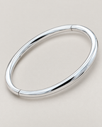 The Talo Open Cuff Bangle — polished silver-tone closed oval with subtle upper and lower joint seams on pale greige; reference-based AI visualization