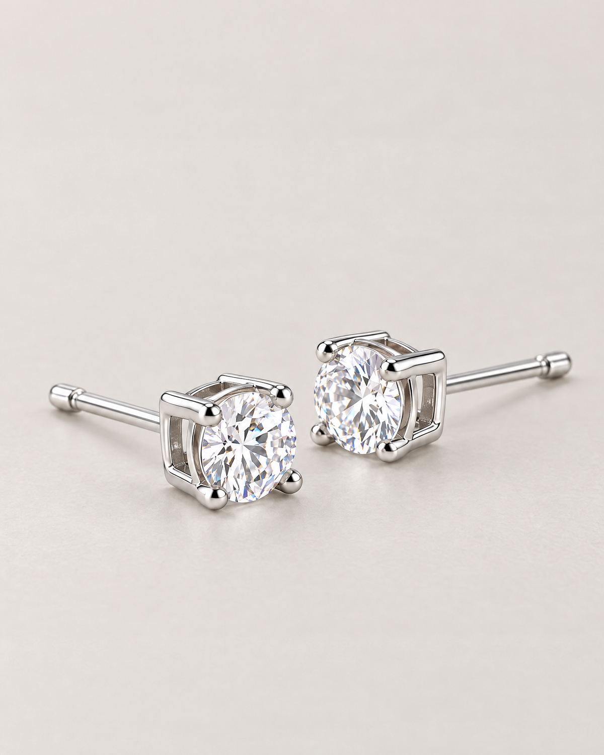 The Neva CZ Stud Earrings — silver-tone low-angle resting pair with clear round stones and visible open settings in a pale-greige studio; reference-based AI visualization.