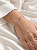 Silver-tone Aelin Paperclip Bracelet with an ivory sleeve and relaxed hand — reference-based AI lifestyle image.