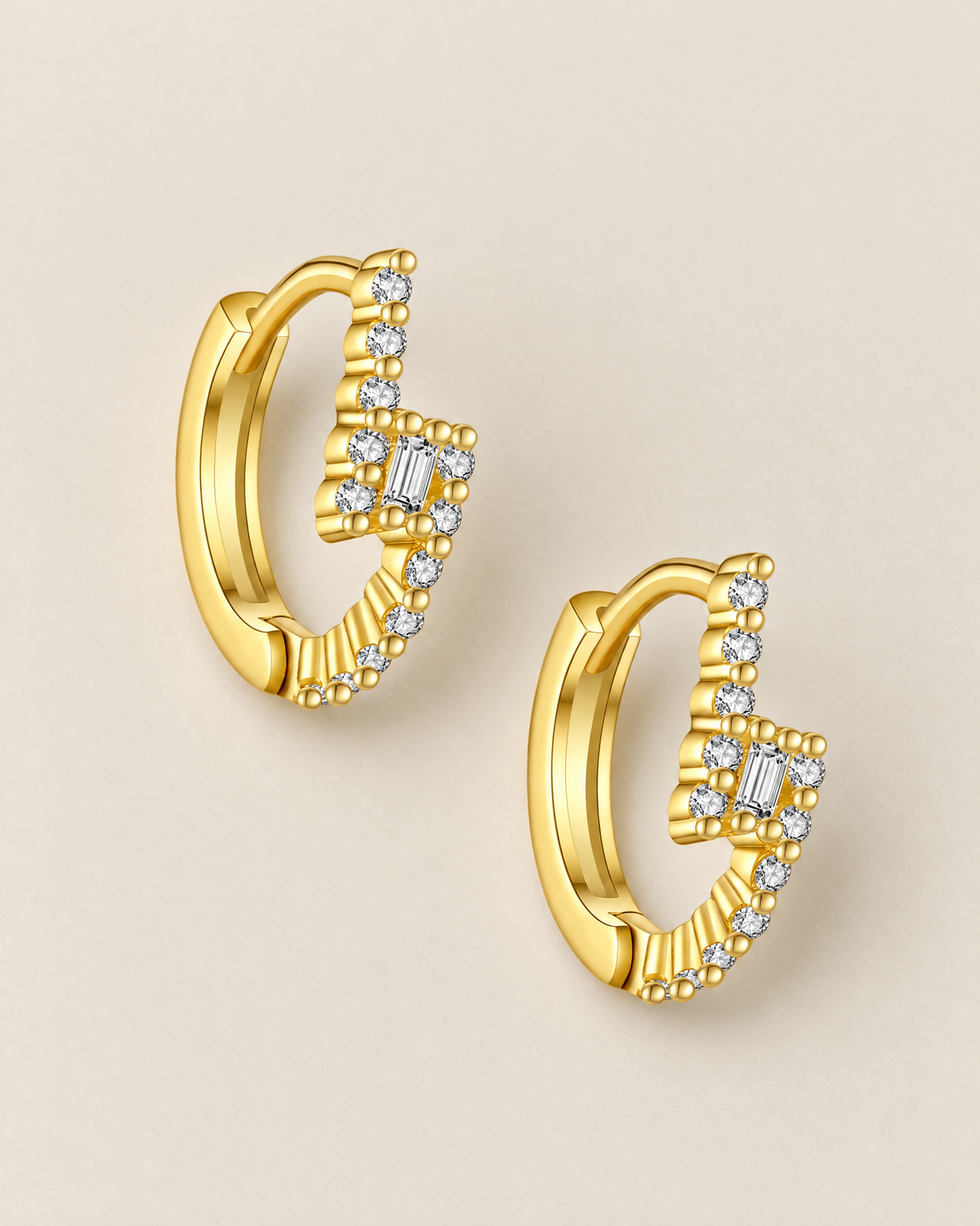 The Veyra Geometric Huggies, separated warm yellow-gold-coloured geometric huggies in a diagonal overhead flat lay with clear rectangular and round stones on pale greige, reference-based AI visualization