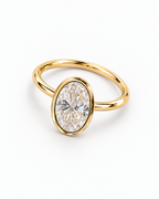 The Esme Bezel-Set Oval Ring in Gold Tone, complete overhead diagonal resting product-only view on a pearl-white studio background, reference-based AI visualization.