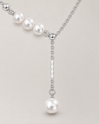 The Freya Pearl Drop Necklace — cool silver-color pearl-accented Y-drop detail on pale greige, reference-based AI visualization