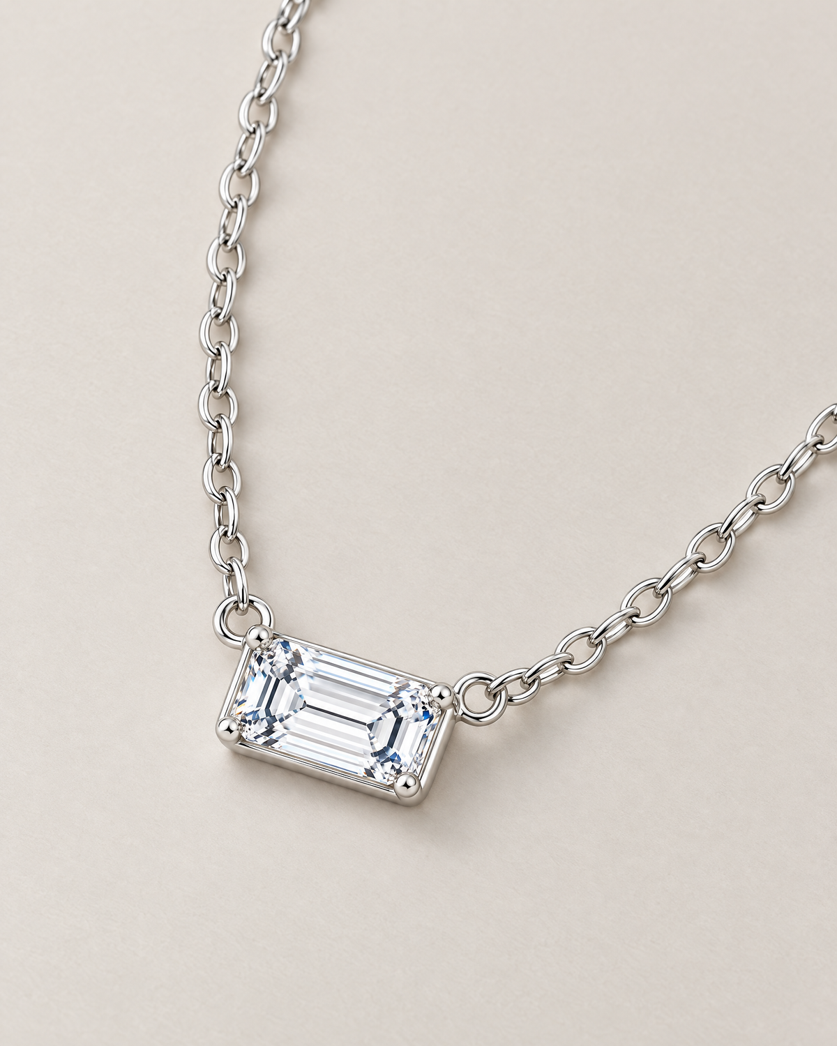 The Mara Geometric CZ Pendant — jewelry-only shallow-oblique view of the horizontal clear rectangular stone and alternating-link chain on pale warm greige; reference-based AI visualization