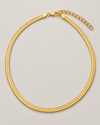 Gold-tone flat herringbone necklace in a tall rounded loop with closure and oval-link extender emphasized at the top on a pale greige studio ground; reference-based AI visualization