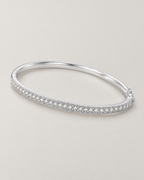 The Maia Pavé Hinge Bangle in polished silver-tone with a clear-stone pavé front band in a diagonal resting lay on pale greige, reference-based AI visualization