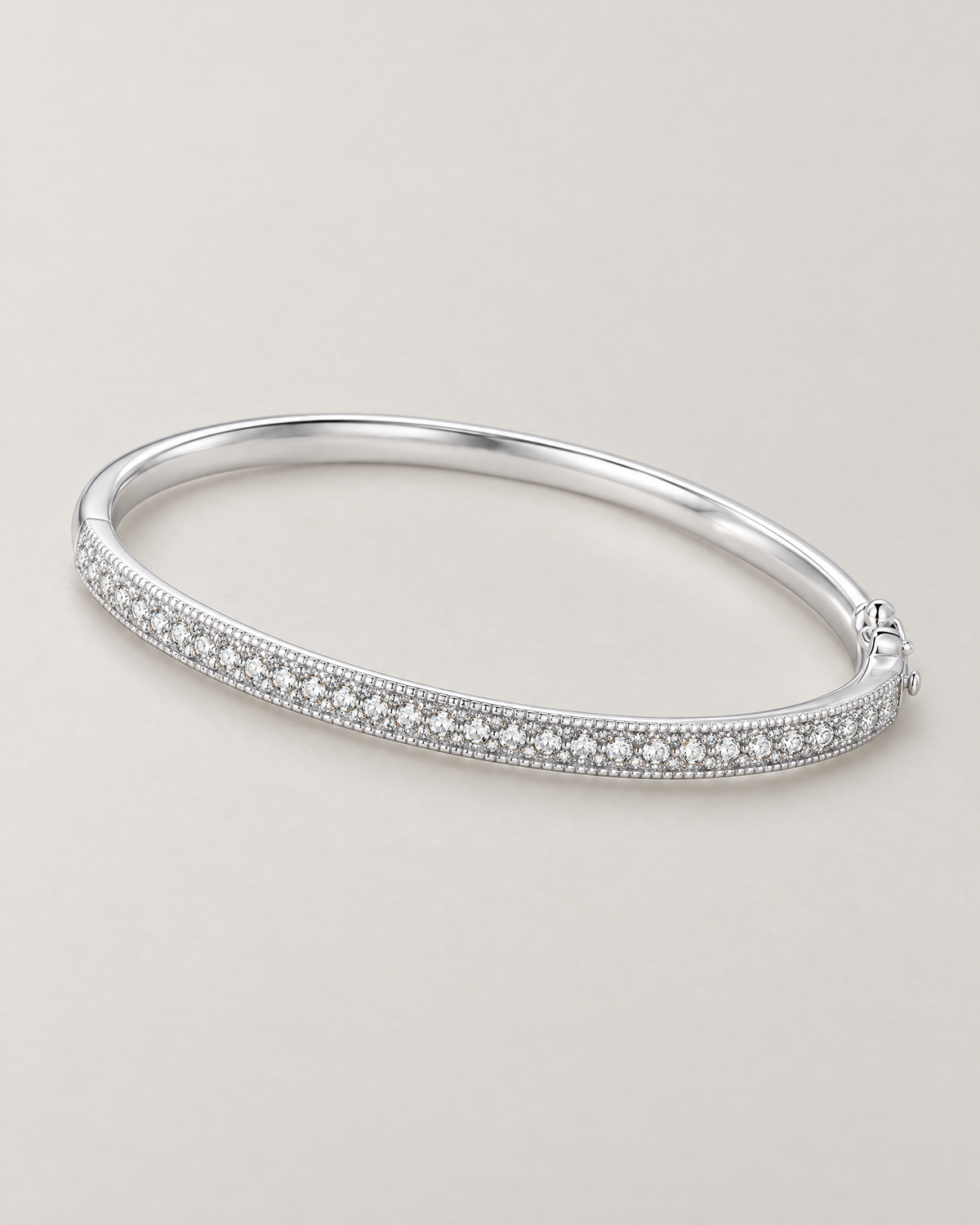 The Maia Pavé Hinge Bangle in polished silver-tone with a clear-stone pavé front band in a diagonal resting lay on pale greige, reference-based AI visualization