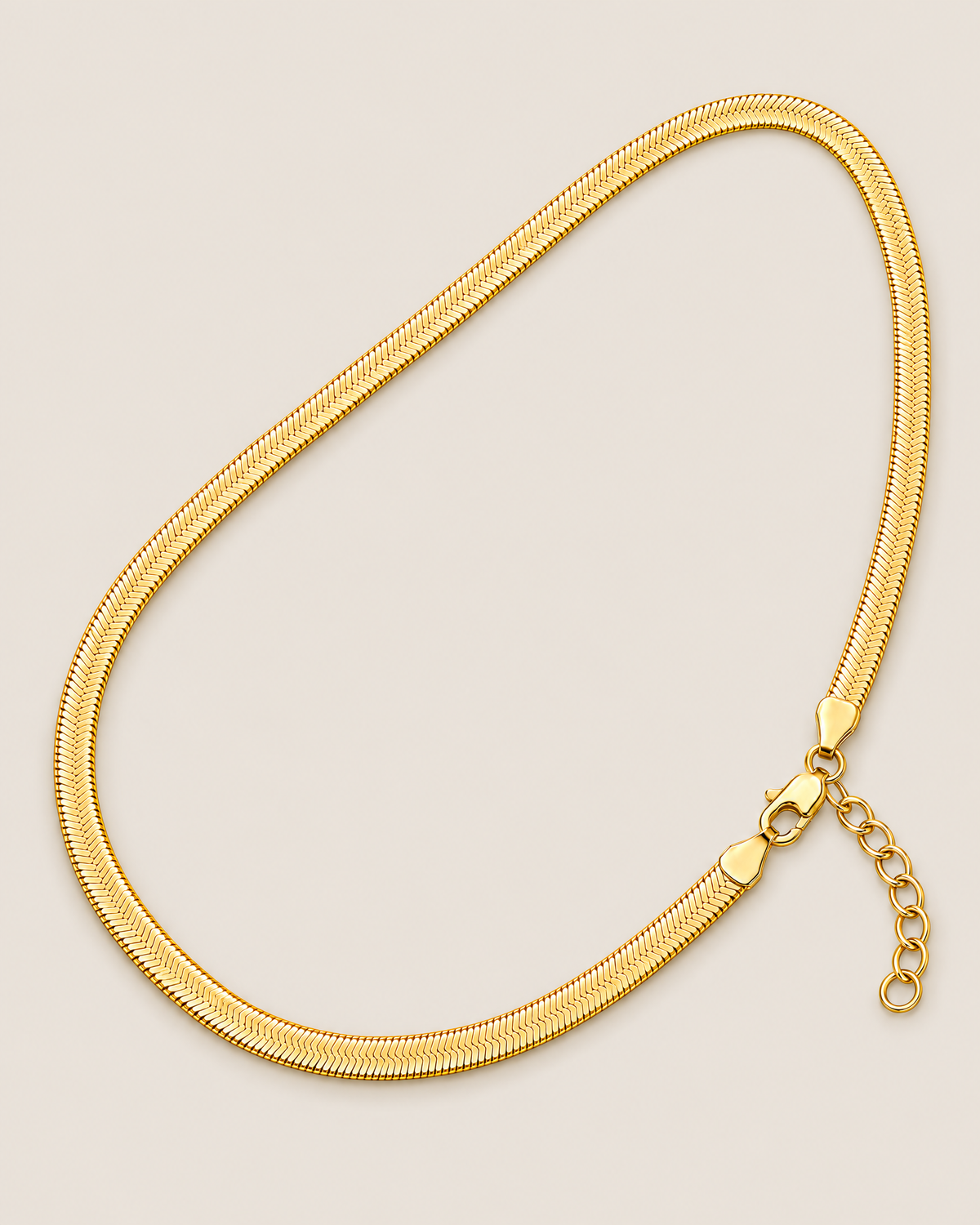 Gold-tone flat herringbone necklace in a diagonal sideways teardrop-shaped loop with clasp and extender at lower right on a pale greige studio ground; reference-based AI visualization