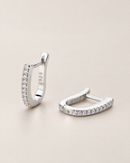 The Aria CZ Hoops — pair of polished silver-colored U-shaped hoops with clear round stone rows, one upright and one resting on pale greige, reference-based AI visualization