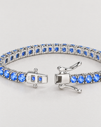 The Orla CZ Tennis Bracelet — open silver-tone box clasp, blue stones and linked underside detail on pale greige — reference-based AI visualization