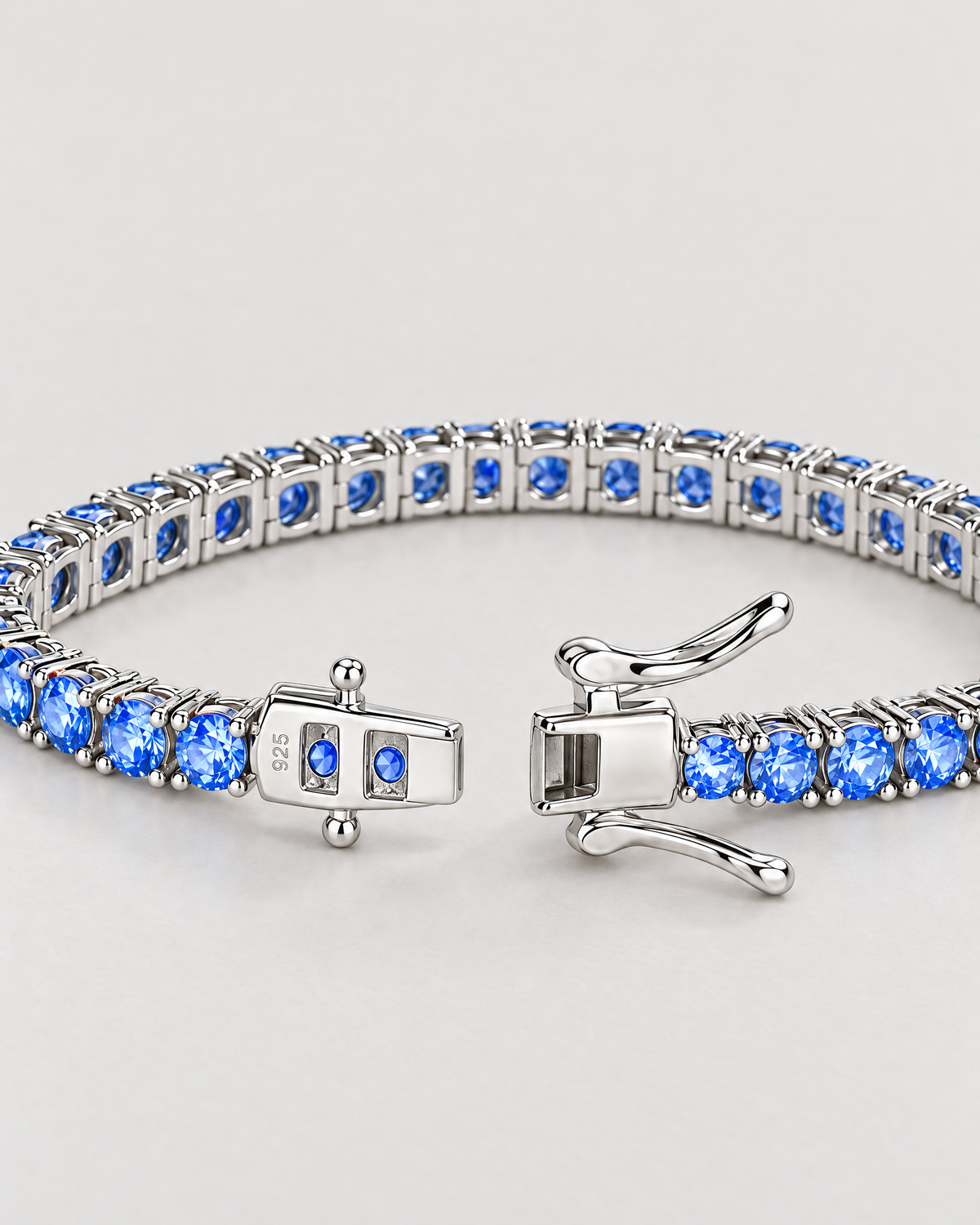 The Orla CZ Tennis Bracelet — open silver-tone box clasp, blue stones and linked underside detail on pale greige — reference-based AI visualization