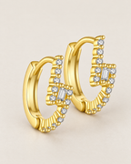 The Veyra Geometric Huggies, offset overlapping warm yellow-gold-coloured geometric huggies with clear rectangular and round stones on pale greige, reference-based AI visualization