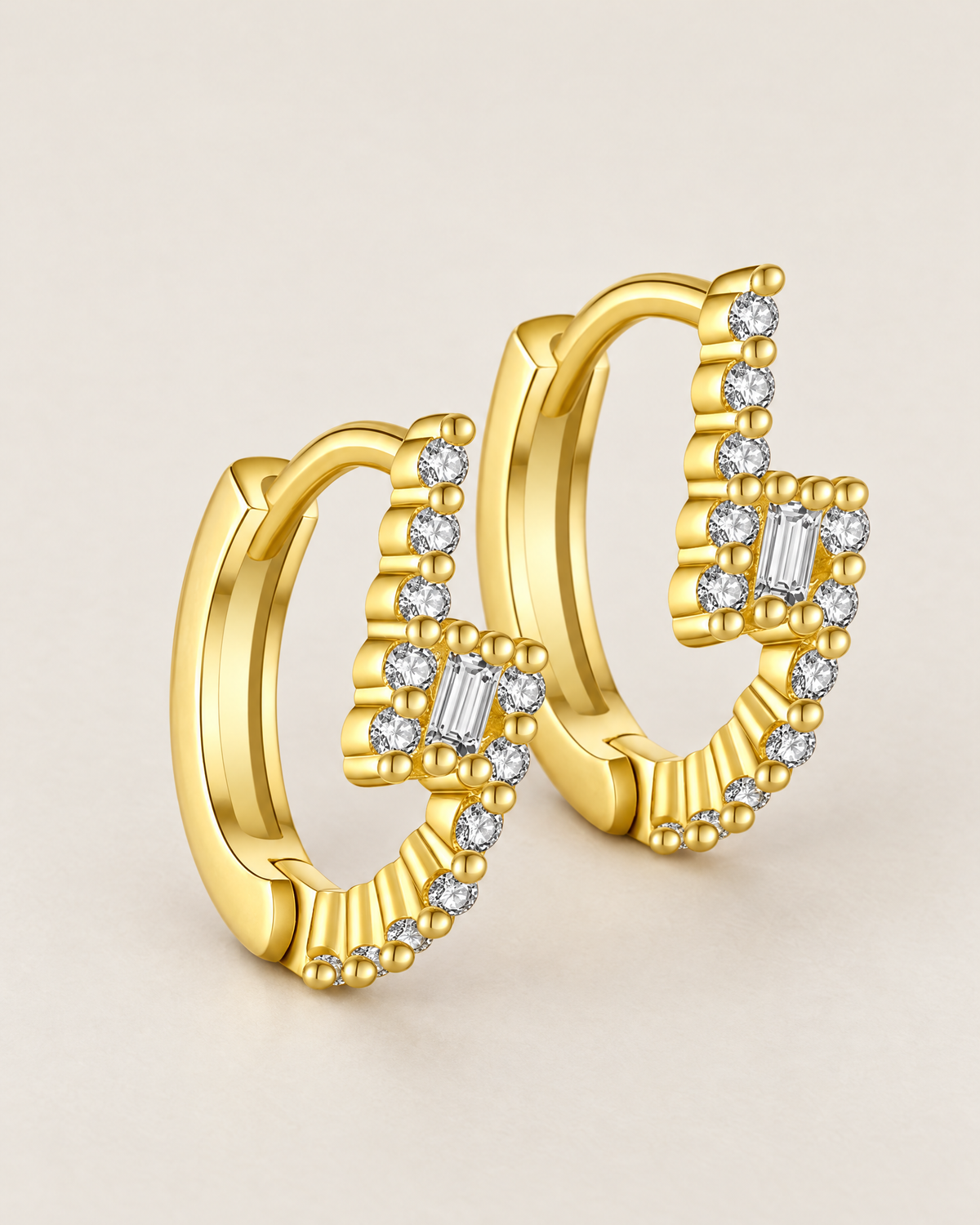 The Veyra Geometric Huggies, offset overlapping warm yellow-gold-coloured geometric huggies with clear rectangular and round stones on pale greige, reference-based AI visualization