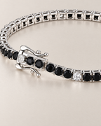 The Signe Black & White CZ Tennis Bracelet in polished silver-tone metal, close on the open clasp, curved safety catches, and black and clear/white round stone line on pale greige, reference-based AI visualization.