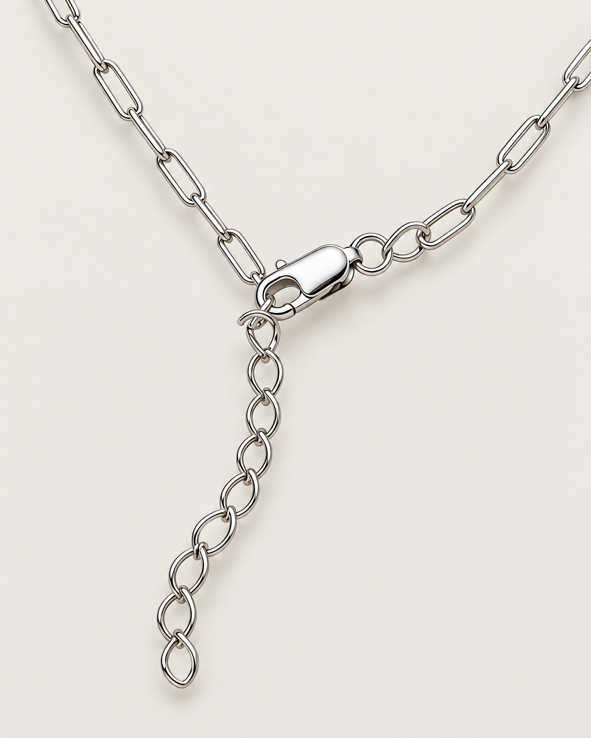 The Tova Dainty Paperclip Chain Necklace — silver-tone clasp and oval-link extender macro on pale greige, reference-based AI visualization.
