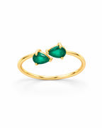 The Tove Green Twin-Pear Ring in polished yellow-gold coloured metal with two green pear-cut stones, upright front three-quarter product-only view on a pearl-white studio background, reference-based AI visualization.