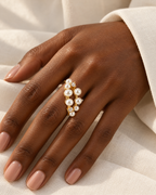 The Ilse Pearl Cluster Ring in observed gold finish, worn on a deep-brown adult hand over ivory linen in warm window light; reference-based AI visualization.