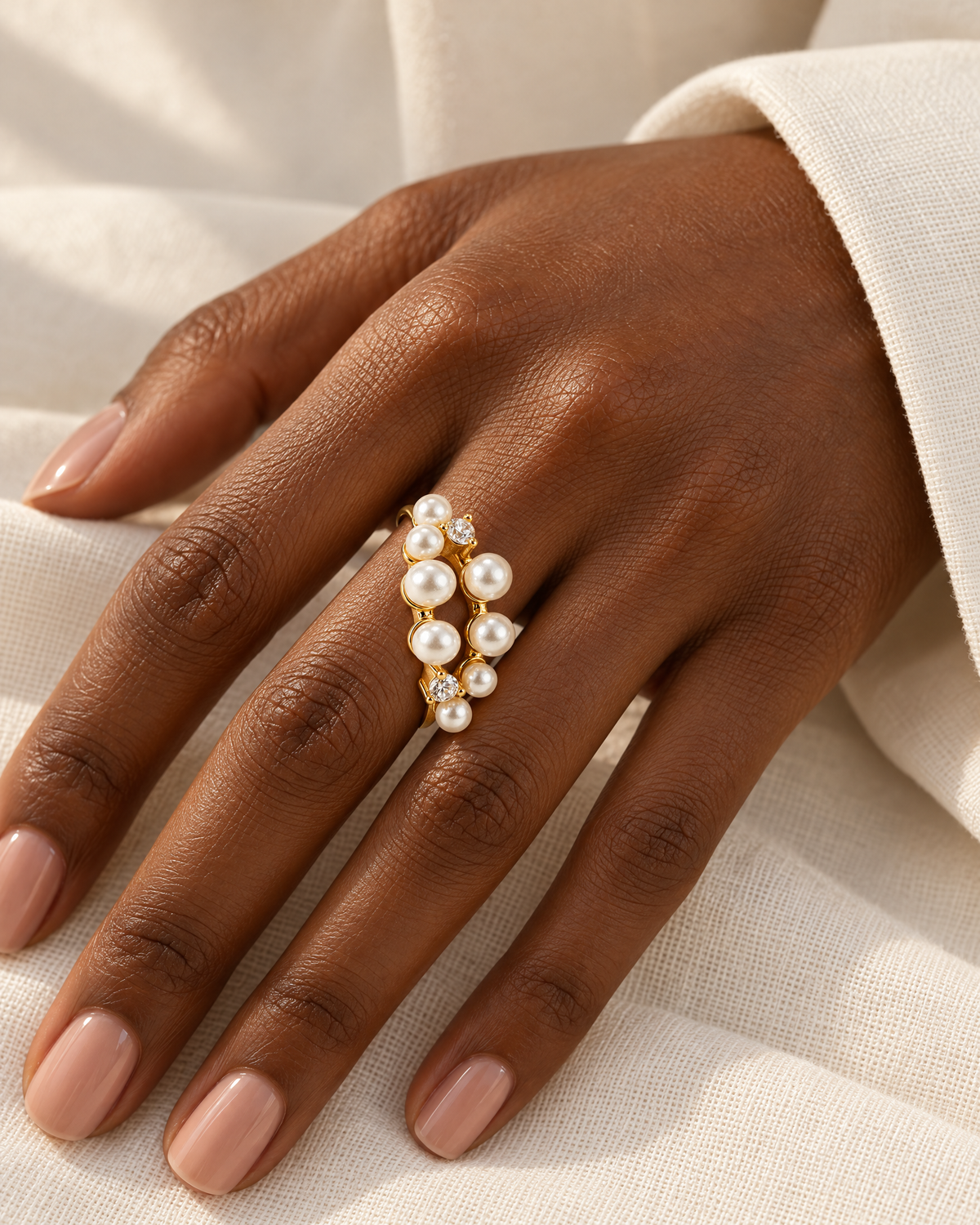 The Ilse Pearl Cluster Ring in observed gold finish, worn on a deep-brown adult hand over ivory linen in warm window light; reference-based AI visualization.