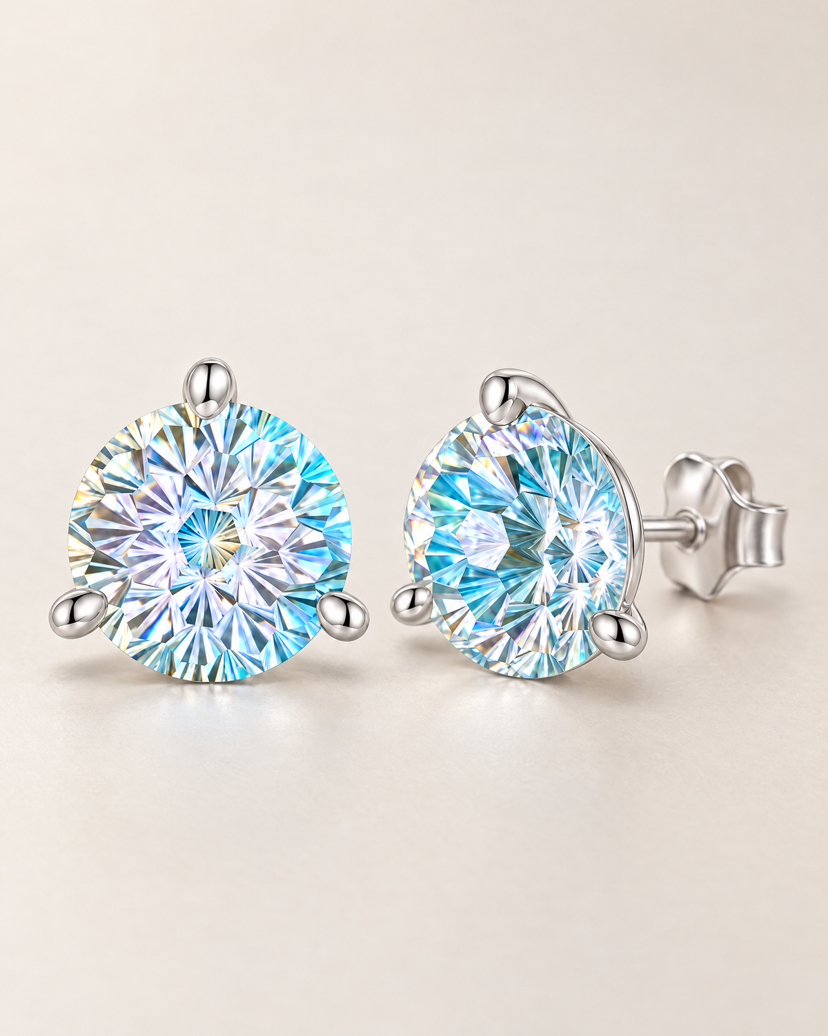 The Frida Firework CZ Stud Earrings: pale clear and aqua-blue rainbow faceted three-prong stud pair with a low profile and butterfly back view on pale greige, reference-based AI visualization