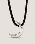 Polished silver-tone crescent pendant on a black braided cord in a centered pale greige studio portrait, reference-based AI visualization