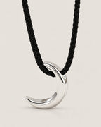 Polished silver-tone crescent pendant on a black braided cord in a centered pale greige studio portrait, reference-based AI visualization