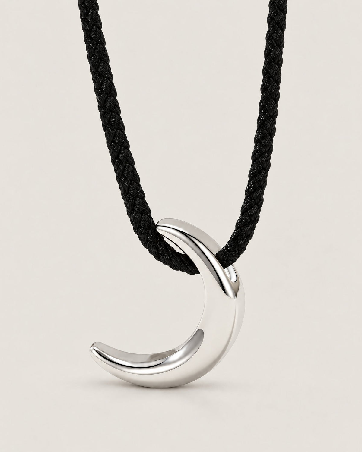 Polished silver-tone crescent pendant on a black braided cord in a centered pale greige studio portrait, reference-based AI visualization
