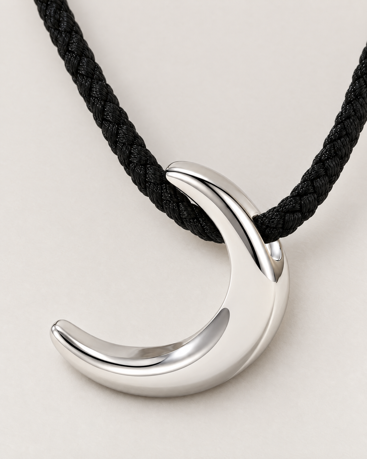 Close detail of a polished crescent pendant and black braided cord passing through its curved top loop, reference-based AI visualization