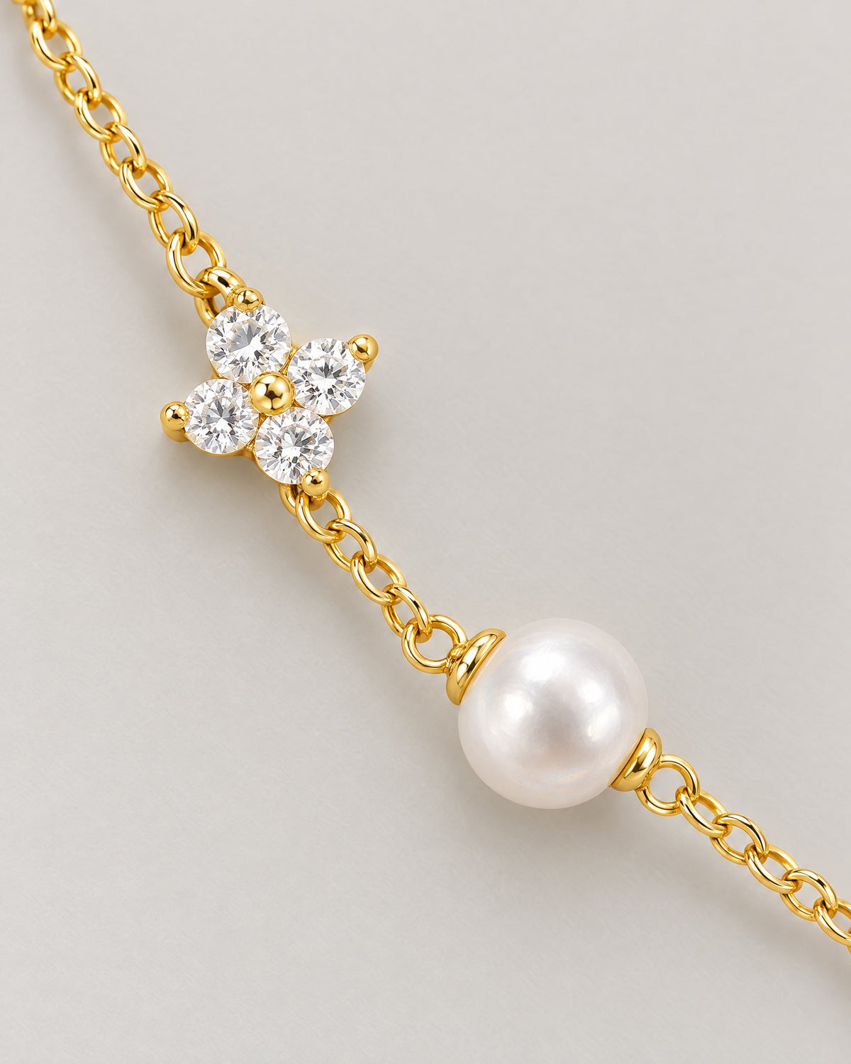 The Amelie Pearl Station Bracelet macro showing a clear four-petal stone station, an off-white pearl-like station and polished yellow-gold-tone chain on pale greige, reference-based AI visualization