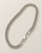 The Liva Mesh Chain Bracelet in a complete silver-tone woven-mesh diagonal oval with lobster clasp and visible 925 ITALY end-cap marking on warm pale greige; reference-based AI visualization.