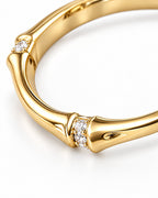 The Ebba Bamboo Band in polished yellow-gold color with clear round stone accents and bamboo-like band detail, macro product-only studio view on a pearl-white background; reference-based AI visualization.