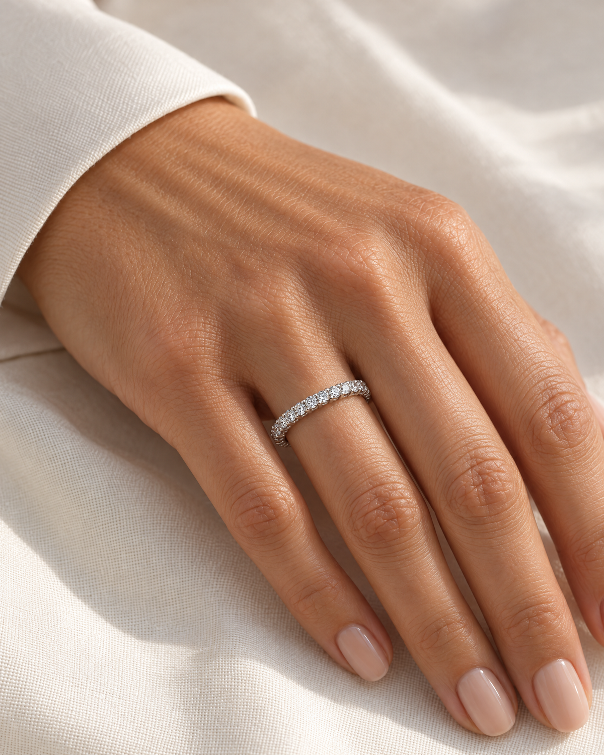 The Vale CZ Eternity Band — bright polished silver-tone clear-stone eternity band worn on an adult woman's hand with ivory linen, reference-based AI visualization