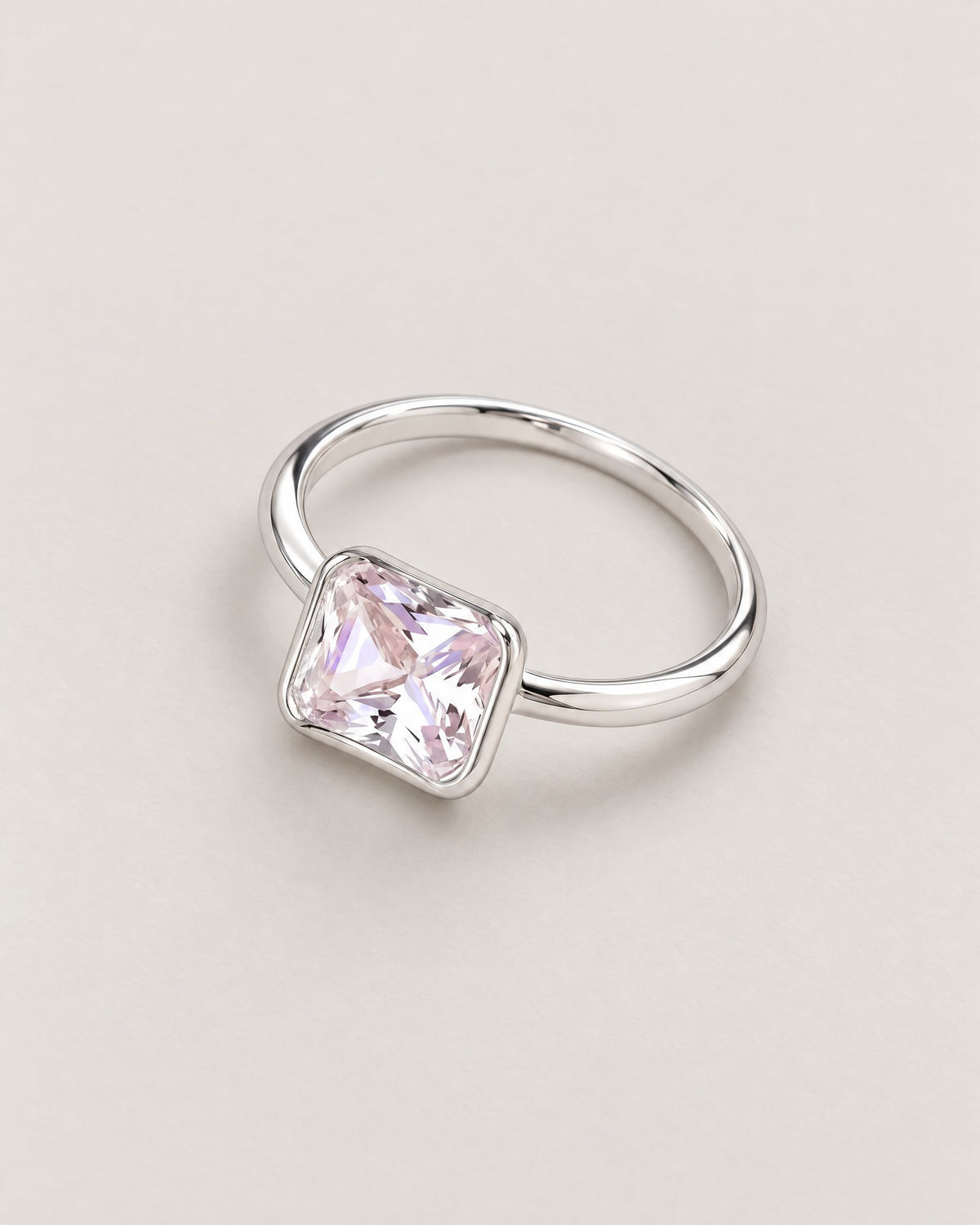 The Eira Square Solitaire Ring in silver finish with one clear faceted square stone in a smooth rounded-square bezel, resting face-up on a diagonal; reference-based AI visualization.