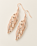 The Sova CZ Drop Earrings — Warm gold-color openwork leaf drop pair in an offset diagonal flat lay on pale greige; reference-based AI visualization