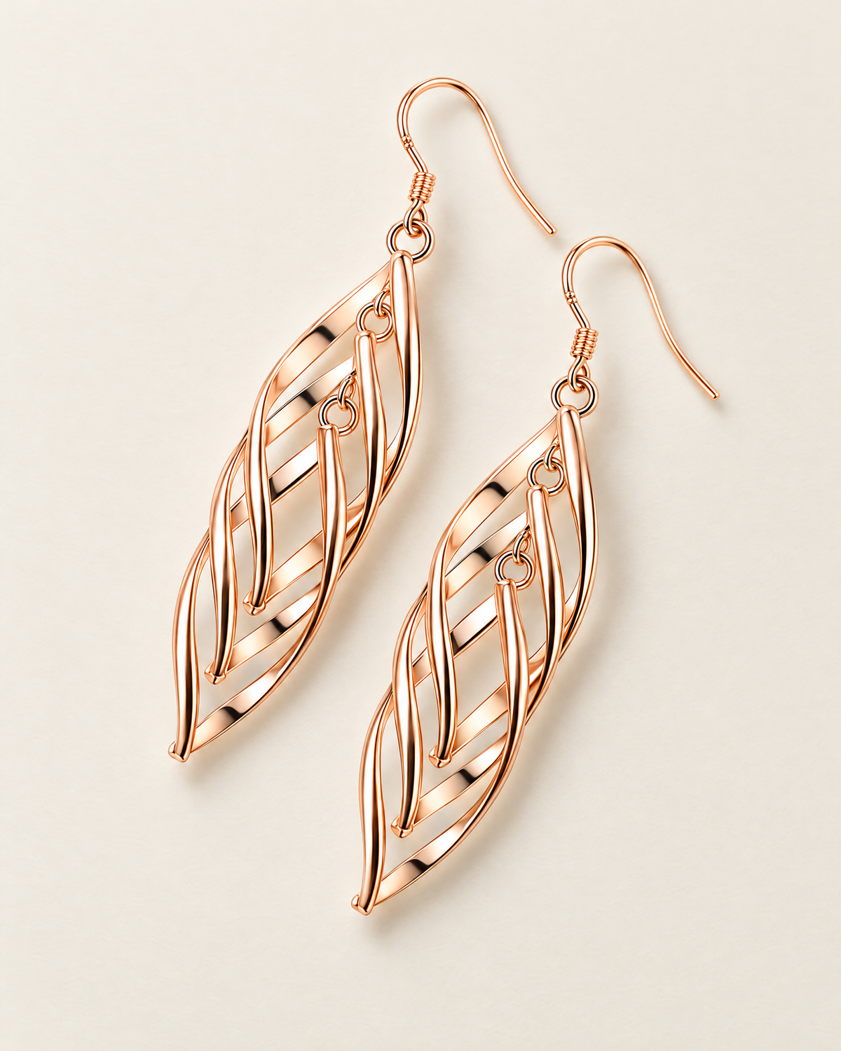 The Sova CZ Drop Earrings — Warm gold-color openwork leaf drop pair in an offset diagonal flat lay on pale greige; reference-based AI visualization