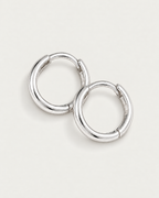 The Kiri Huggie Hoops — silver pair — diagonal flat lay on pale greige, product-only; reference-based AI visualization.