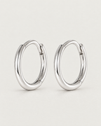 The Kiri Huggie Hoops — silver pair — angled standing pair on pale greige, product-only; reference-based AI visualization.