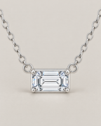 The Mara Geometric CZ Pendant — jewelry-only straight-on detail of the horizontal clear rectangular stone, four corner prongs, side rings, and short alternating-link chain sections on pale warm greige; reference-based AI visualization
