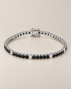 The Signe Black & White CZ Tennis Bracelet in polished silver-tone metal, shown as a full oval with repeating black and clear/white round stones and a box clasp on pale greige, reference-based AI visualization.