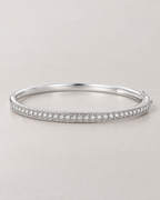 The Maia Pavé Hinge Bangle in polished silver-tone with a clear-stone pavé front band in a low-angle resting view on pale greige, reference-based AI visualization