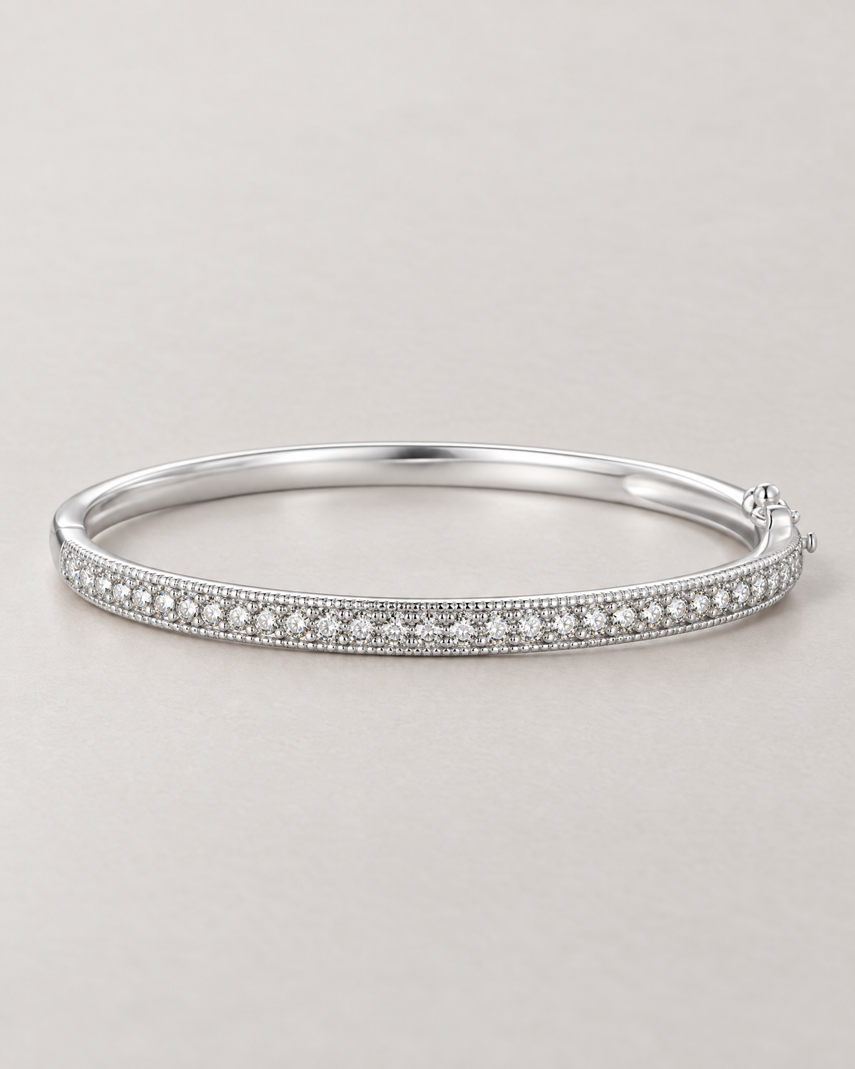 The Maia Pavé Hinge Bangle in polished silver-tone with a clear-stone pavé front band in a low-angle resting view on pale greige, reference-based AI visualization