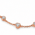 The Dahlia S925 Heart Bracelet in warm rose-gold-toned metal, close on clear round and heart stone stations linked by chain on pale greige, reference-based AI visualization.