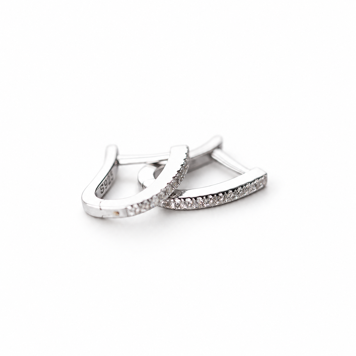 The Aria CZ Hoops — overlapping polished silver-colored U-shaped hoops with clear round stone rows on pale greige, reference-based AI visualization
