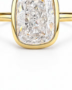 The Tilde Bezel Ring in polished yellow-gold tone with one clear faceted rounded-rectangle stone in a lower bezel detail macro on pearl-white — reference-based AI visualization