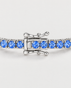 The Orla CZ Tennis Bracelet — closed silver-tone clasp with adjacent blue four-prong settings on pale greige — reference-based AI visualization
