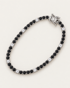 The Signe Black & White CZ Tennis Bracelet in polished silver-tone metal, arranged in an overhead diagonal oval with repeating black and clear/white round stones on pale greige, reference-based AI visualization.
