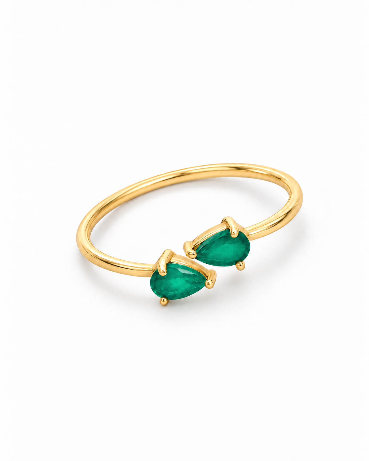 The Tove Green Twin-Pear Ring in polished yellow-gold coloured metal with two green pear-cut stones in a diagonal flat lay on a pearl-white studio background, reference-based AI visualization.