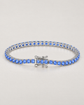 The Orla CZ Tennis Bracelet — polished silver-tone blue-stone tennis bracelet in a complete three-quarter oval on pale greige — reference-based AI visualization