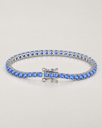 The Orla CZ Tennis Bracelet — polished silver-tone blue-stone tennis bracelet in a complete three-quarter oval on pale greige — reference-based AI visualization