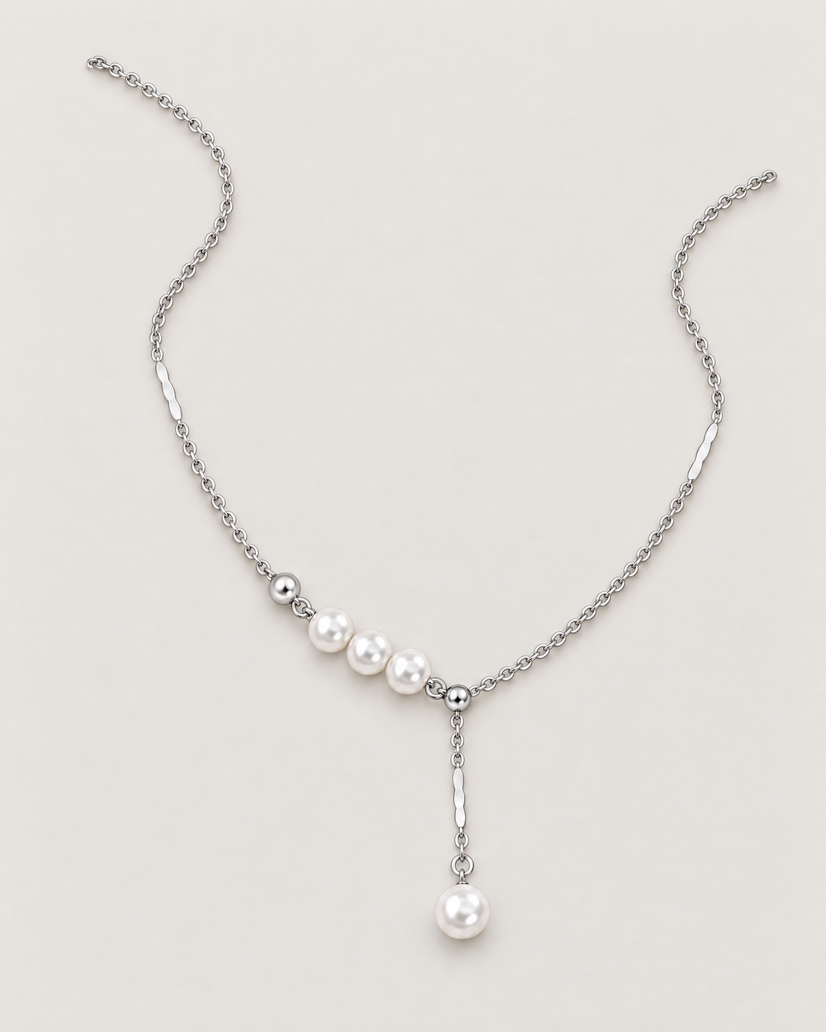 The Freya Pearl Drop Necklace — cool silver-color cable chain in a relaxed open-U lay with three white pearl-like accent beads and a single pearl-like drop on pale greige, reference-based AI visualization